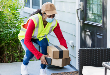 A delivery person wearing a visibility vest places some packages on a porch.