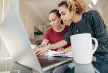 Two women review something on their laptop together while at their kitchen table.