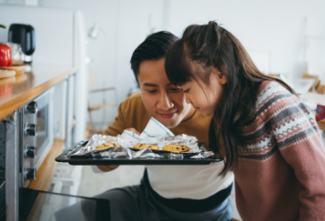 A father and daughter lean down to smell a sheet of freshly baked cookies that just came out of the oven.