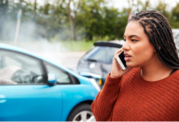 Woman on phone standing in front of a car accident.