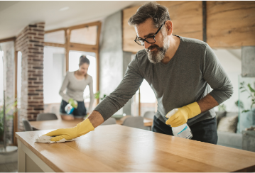 A person cleans a table with a rag and a cleaner.