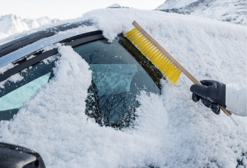 A hand using a snow brush to clear snow off of a car window.