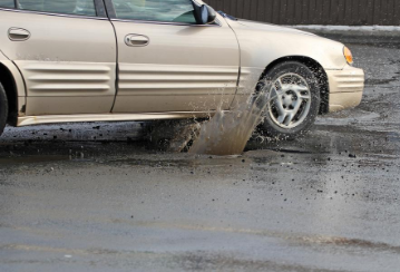 Car driving through a deep pothole.