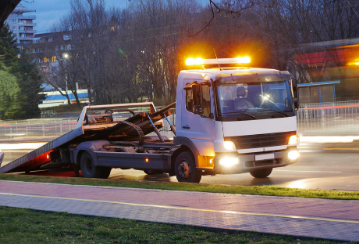 A tow truck sits by the side of the road with its lights on at dusk.